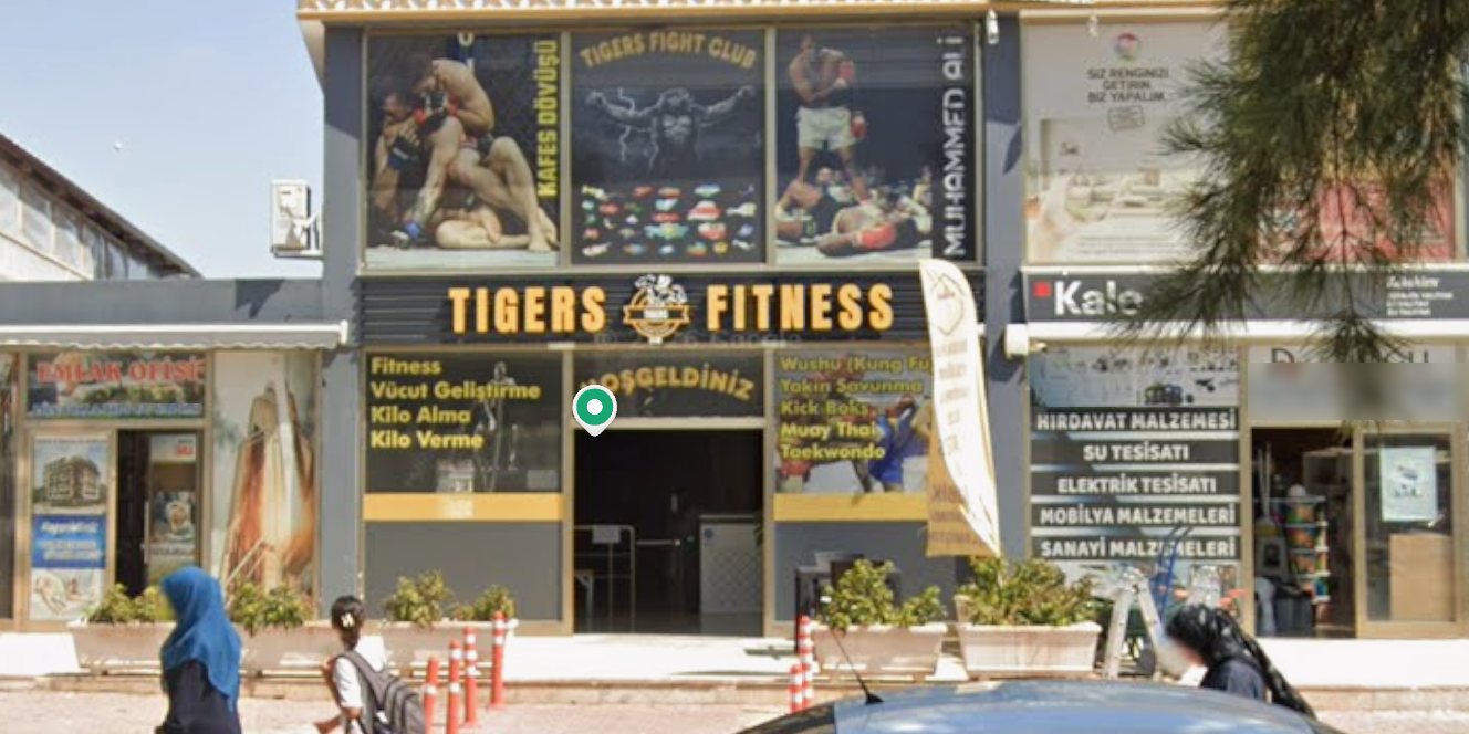Sokağın karşısından Tigers Fitness binası: üst katta Fight Club posterleri, altta sarı Tigers Fitness tabelası